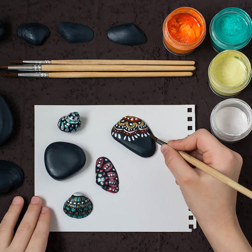person painting design onto smooth rocks