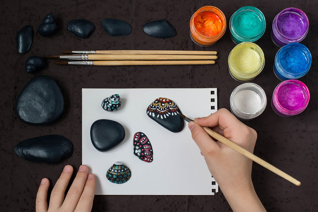 person painting design onto smooth rocks