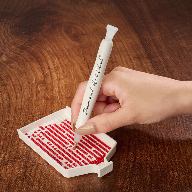 A pen picking up a red diamond from a ridged tray.
