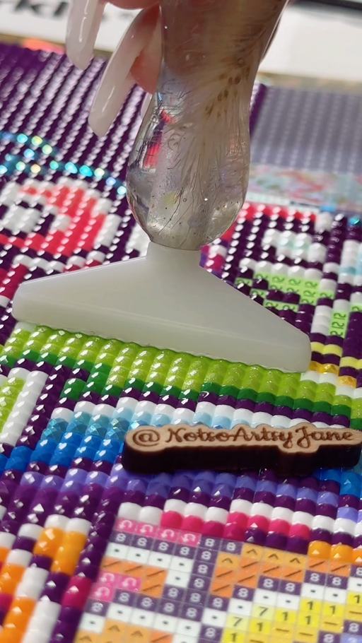 A wide applicator placing lime-green diamonds in a crisp row on a colorful canvas