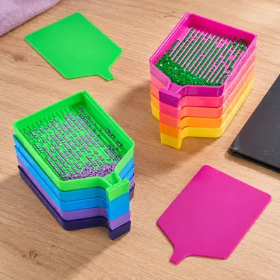 Stacks of rainbow diamond painting trays on a warm wooden craft table.