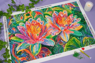 A colorful water lily diamond painting with greenery, a candle, a pen and a diamond tray.